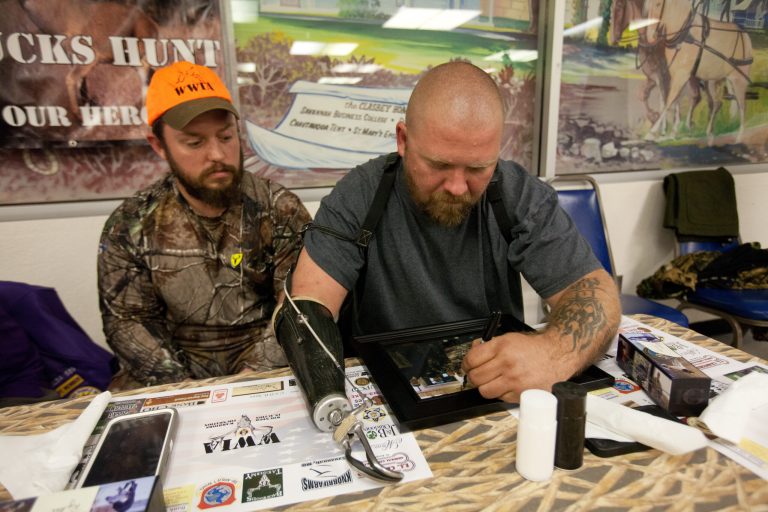Iraq War veteran Dave Sterling, right, signs a group portrait taken the day before at Napier Hunt Club as Iraq War veteran Ronald Ryker observes at the annual fundraiser dinner for Wounded Warriors in Action's Ducks N Bucks weekend at Clasbey Community Center in Savannah, Mo., Friday, Nov. 22, 2013. Both veterans have purple hearts. (AP Photo/St. Joseph News-Press, Sait Serkan Gurbuz)