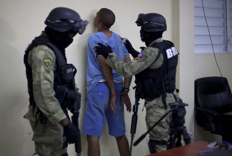 Clifford Brandt, center, is placed against the wall at the police station after his arrest in Port-au-Prince, Haiti, Tuesday, August 12, 2014. Brandt was taken into custody in the Haitian town of Cornillon, near the border with the Dominican Republic, Communications Minister Rudy Heriveaux said. (AP Photo/Dieu Nalio Chery)