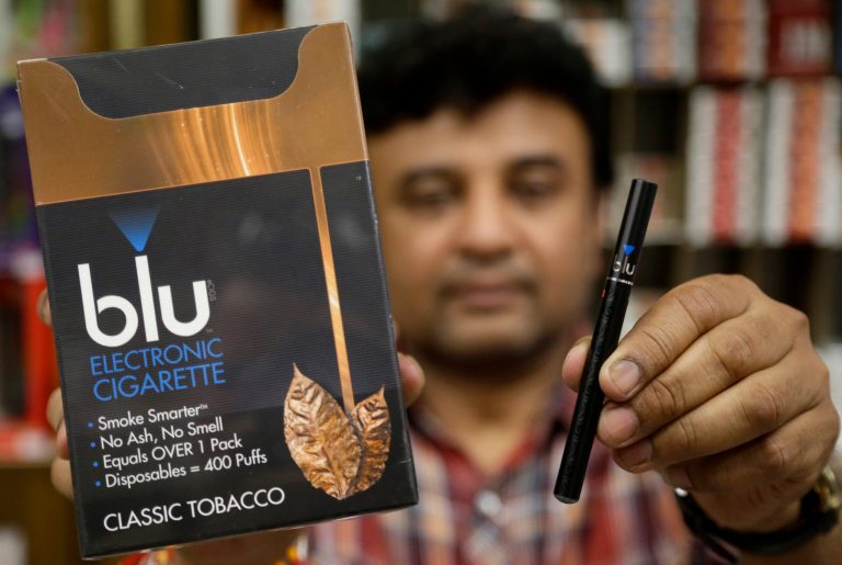 Sales clerk Sam Patel, of Waltham, Mass., displays a blu e-cigarette, right, and a container of the e-cigarettes, left, at a shop, Wednesday, May 21, 2014, in Brookline, Mass. Regulations on e-cigarettes are likely to die under President-elect Trump. (AP Photo/Steven Senne)