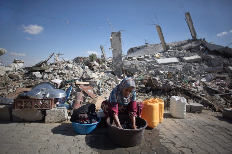 In this Wednesday, Oct. 1, 2014 photo, Palestinian woman washes clothes as she sits in front of the rubble of her family house in Khuzaa, southern of Gaza Strip. More than five weeks after the Israel-Hamas war in the Gaza Strip, tens of thousands of people whose homes were destroyed or badly damaged in the fighting still live in classrooms, storefronts and other crowded shelters. Yet despite their pressing needs, reconstruction efforts appear stymied by a continued Israeli-Egyptian border blockade of Gaza and an unresolved power struggle between the Islamic militant group Hamas and Western-backed Palestinian President Mahmoud Abbas. (AP Photo/Khalil Hamra)
