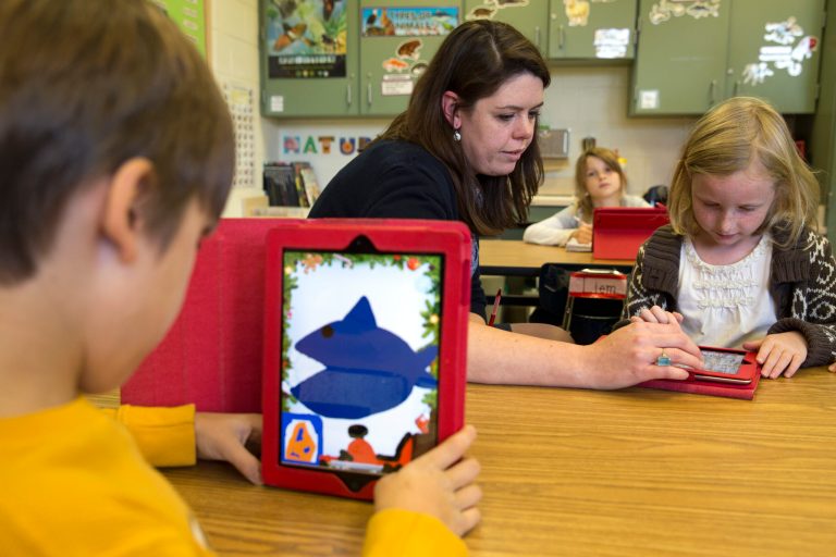 This photo taken Nov. 25, 2013 shows second grade teacher Heather Black working with Ingrid Soracco, 7, right, on her e-book assignment using an iPad at Jamestown Elementary School in Arlington, Va. Needed to keep a school building running these days: Water, electricity _ and broadband. Interactive digital learning on laptops and tablets is, in many cases, replacing traditional textbooks. Students are taking computer-based tests instead of fill-in-the bubble exams. Teachers are accessing far-off resources for lessons. (AP Photo/Jacquelyn Martin)