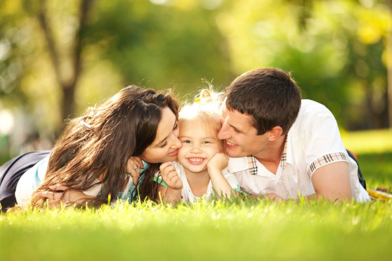 Happy mother and father kissing their daughter in the park