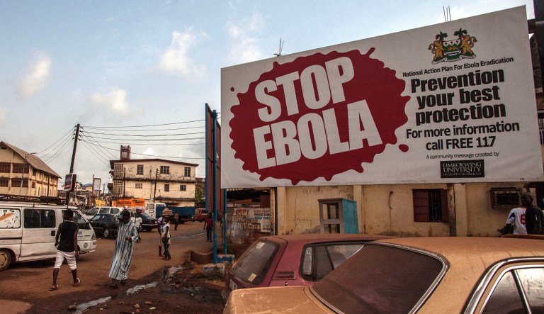 FILE- In this file photo taken on Friday, Jan. 15, 2016, people pass a banner reading 'STOP EBOLA' forming part of Sierra Leone's Ebola free campaign in the city of Freetown, Sierra Leone. A second case of Ebola emerged Thursday Jan. 21, 2016 in Sierra Leone after health officials thought the epidemic was over, with a close relative of the first victim testing positive for the virus that has killed more than 11,000 people, authorities said.