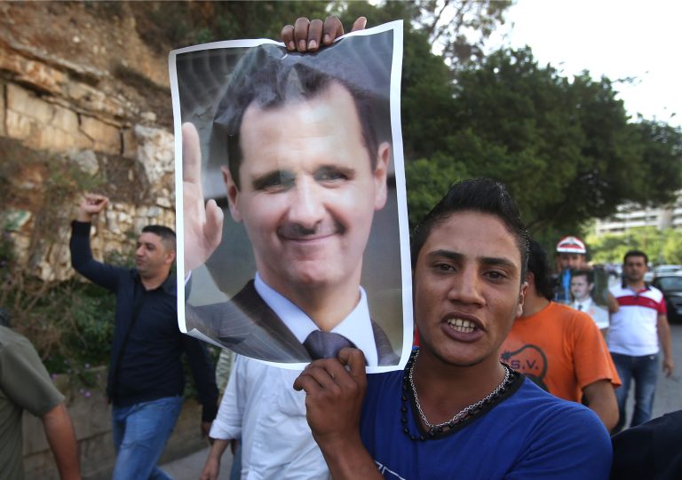 Syrian citizens who live in Lebanon shout slogans, background, as one carries a portrait of Syrian President Bashar Assad, as they walk towards to the Syrian embassy to ballot their vote for their presidential elections, in Baabda east of Beirut, Lebanon, Wednesday May 28, 2014. Thousands are flocking to the Syrian embassy in Lebanon as expat voting starts ahead of Syria's June 3 presidential election. (AP Photo/Hussein Malla)