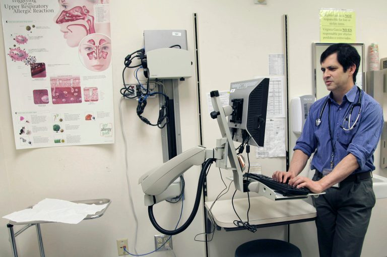 In this July 11, 2014 photo, primary care doctor John Guerreiro checks on the records of a patient at a clinic run by the Virginia Garcia Memorial Health Center in Beaverton, Ore. The center comprised of nine clinics in northwestern Oregon, serveing 36,000 patients in Washington and Yamhill has been overwhelmed under the Affordable Health Care Act's Medicaid expansion. It has closed to new enrollees and is working through a backlog to assign thousands of patients to a doctor. (AP Photo/Gosia Wozniacka)
