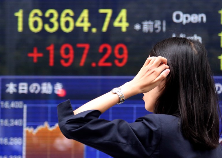 A woman walks by an electronic stock board of a securities firm in Tokyo, Thursday, Sept. 25, 2014. Asian stock markets were mostly higher Thursday after a surge in new home sales in the U.S. bolstered sentiment. But gains were limited by worries about Europe's stagnant economy and violence in Iraq and Syria. (AP Photo/Koji Sasahara)