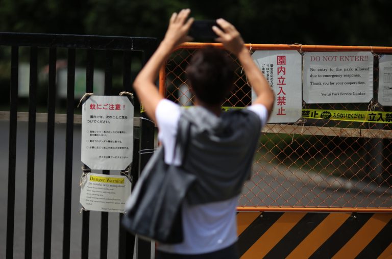 A visitor takes photos of some mosquitoes warning posters at closed gate of Yoyogi Park in Tokyo Friday, Sept. 5, 2014. Yoyogi Park, a popular park in downtown Tokyo, has been closed temporarily after dozens of cases of dengue fever were contracted by people who visited the area. (AP Photo/Eugene Hoshiko)