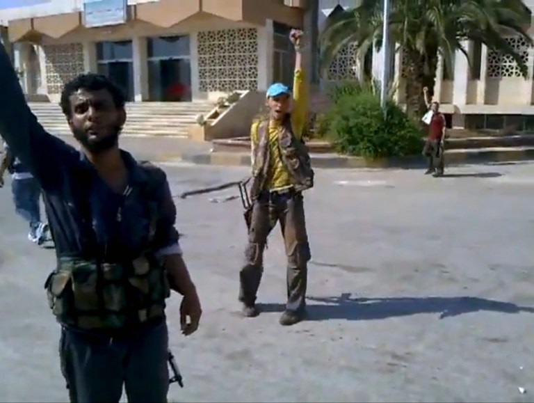 This image made from amateur video released by Shaam News Network and accessed by the Associated Press Thursday, July 19, 2012 purports to show Syrian rebels cheering as a comrade defaces a poster of President Bashar Assad at the Bab al-Hawa border crossing with Turkey. Syrian President Bashar Assad made his first appearance Thursday since a bomb killed some of his top lieutenants, looking calm and composed on state TV even as his forces turned parts of Damascus into combat zones and rebels seized two of the country's border crossings. (AP Photo/Shaam News Network via AP video)