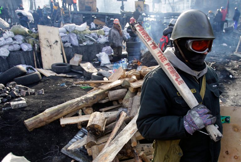 A protester guards the barricade in front of riot police in Kiev, Ukraine, Monday, Jan. 27, 2014. Ukraine's justice minister is threatening to call for a state of emergency unless protesters leave her ministry building, which they occupied during the night. The seizure of the building early Monday underlined how anti-government demonstrators are increasingly willing to take dramatic action as they push for the president's resignation and other concessions. Protesters now occupy four sizable buildings in downtown Kiev, including the city hall. (AP Photo/Darko Vojinovic)