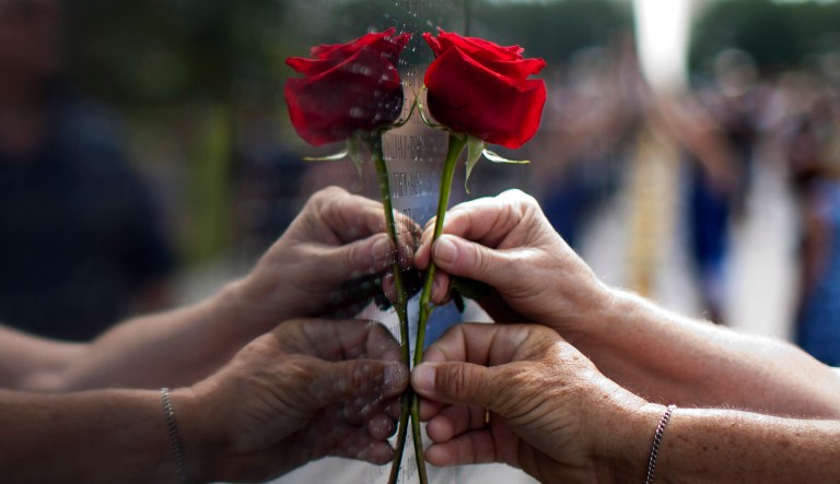 Carol Bates, of Calif., top hand, is guided as she is holds a rose against the Vietnam Veterans Memorial in Washington, Sunday, June 18, 2017, during the Vietnam Veterans Memorial Fund's annual Father's Day Rose Remembrance in honor of Father's Day. (AP Photo/Carolyn Kaster)