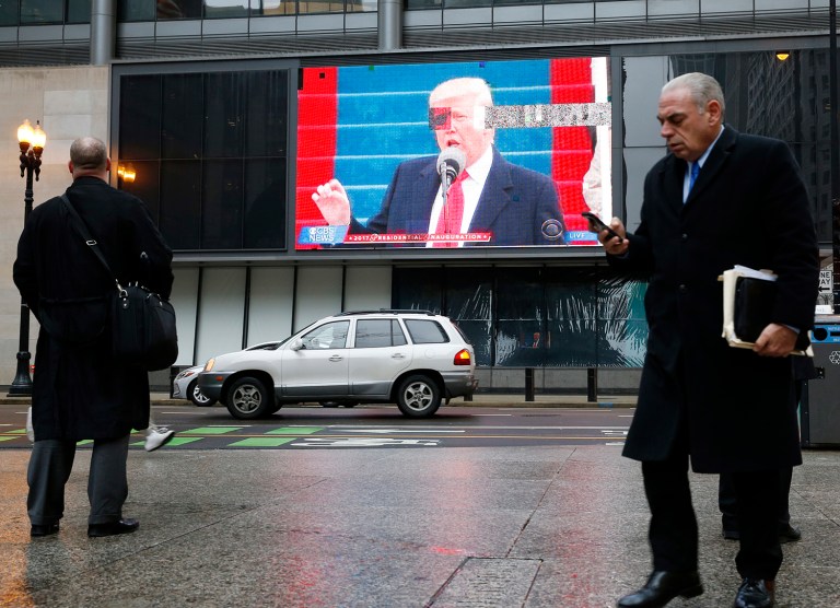 People walk by a big screen tv as it displays the presidential inauguration of Donald Trump in downtown Chicago Friday, Jan. 20, 2017. (AP Photo/Nam Y. Huh)