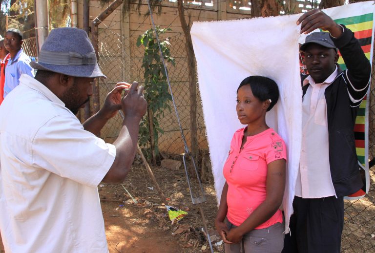 In this photo taken Monday, Aug. 5, 2014, a woman has her passport photos taken outside the passport office in Harare. People queue for hours before the offices open in the hope of securing a passport that will allow  them to escape their country's dearth  of opportunities and  search for work abroad.   (AP Photo/Tsvangirayi Mukwazhi)