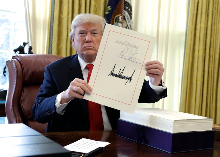 President Donald Trump displays the $1.5 trillion tax overhaul package he had just signed, Friday, Dec. 22, 2017, in the Oval Office of the White House in Washington. Trump touted the size of the tax cut, declaring to reporters in the Oval Office before he signed it Friday that 