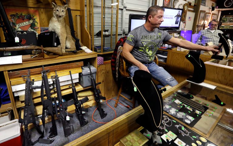 Johnny's Auction House owner John West prepares items, including a line of assault rifles behind him, for auction where the company handles gun sales for both civilians and a half dozen police departments and the Lewis County Sheriff's Office, in Rochester, Wash. (AP Photo/Elaine Thompson)
