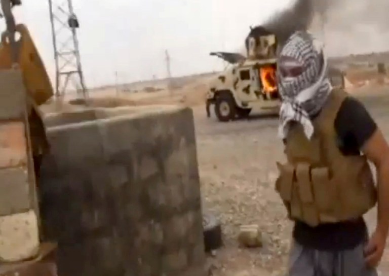 This Image made from video posted by Iraqi0Revolution, a group supporting the al Qaeda breakaway Islamic State of Iraq and the Levant (ISIL) on Wednesday, June 11, 2014, which has been verified and is consistent with other AP reporting, shows a militant standing in front of a burning Iraqi Army Humvee in Tikrit, Iraq. (AP Photo/Iraqi0Revolution via AP video, File)