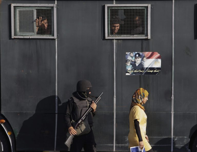 An Egyptian woman walks past a vehicle carrying anti-riot police officers deployed to secure a protest against sexual harassment in Cairo, Egypt, Saturday, June 14, 2014. Egypt's top prosecutor referred Saturday 13 men to trial for attempted rape and assault of women during public rallies in Cairo's iconic Tahrir square, the first implementation of tough new penalties against rampant sexual violence, the state news agency reported. Arabic reads, 