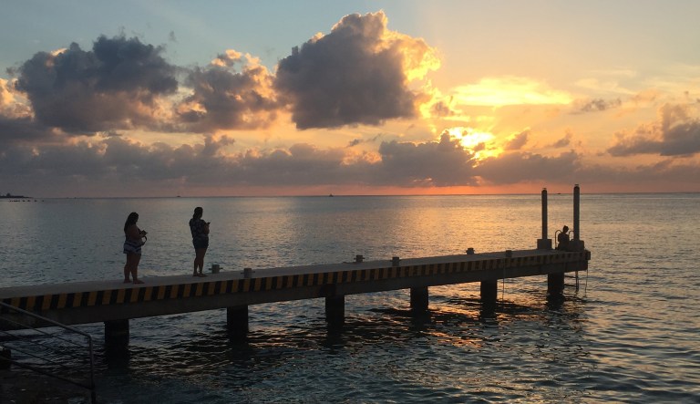 This 2017 photo taken in Cozumel, Mexico shows people on a pier at sunset over the Caribbean. The embassy issued a safety alert Friday warning U.S. citizens visiting the area to exercise caution. U.S. government employees are barred from using tourist ferries that run between Cozumel and Playa del Carmen while an investigation is ongoing regarding undetonated explosives. (AP Photo/Marjorie Miller)