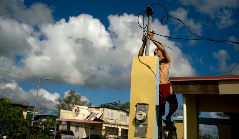 In this Friday, Oct. 13, 2017 photo, a resident tries to connect electrical lines downed by Hurricane Maria in preparation for when electricity is restored in Toa Baja, Puerto Rico. About 75 percent of Puerto Rico remains without power. (AP Photo/Ramon Espinosa)