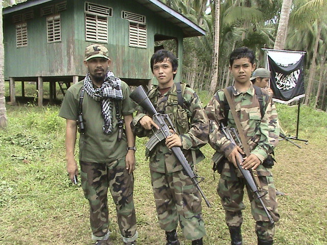 In this undated photo made available, Wednesday, June 11, 2014, by Philippine National Police in Manila, Philippines,  Khair Mundos, left, a top commander of the Abu Sayyaf extremist group who is on the U.S. list of most-wanted terrorists and has once acknowledged receiving al-Qaida funds to finance local bombings, poses with his comrades while training at their camp on Mindanao island in southern Philippines. Philippine security officials said Mundos was arrested in a slum community near Manila's international airport but it was not immediately clear why he was in the capital. The military and police have been hunting him for his alleged involvement in bombings and kidnappings. (AP Photo/Philippine National Police)