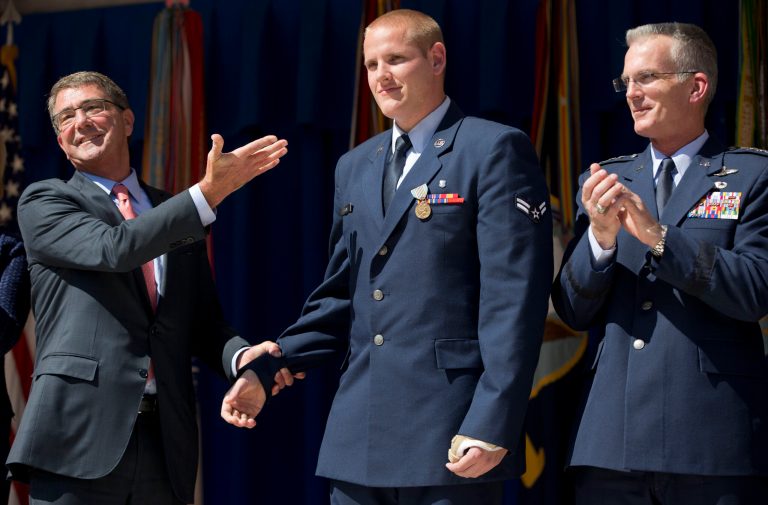 Defense Secretary Ash Carter, left, gestures towards Airman 1st Class Spencer Stone, center, before awarding Stone with the Airman's Medal and Purple Heart medal, during a ceremony with Joint Chiefs Vice Chairman Gen. Paul Selva, right, at the Pentagon. (AP Photo/Pablo Martinez Monsivais)