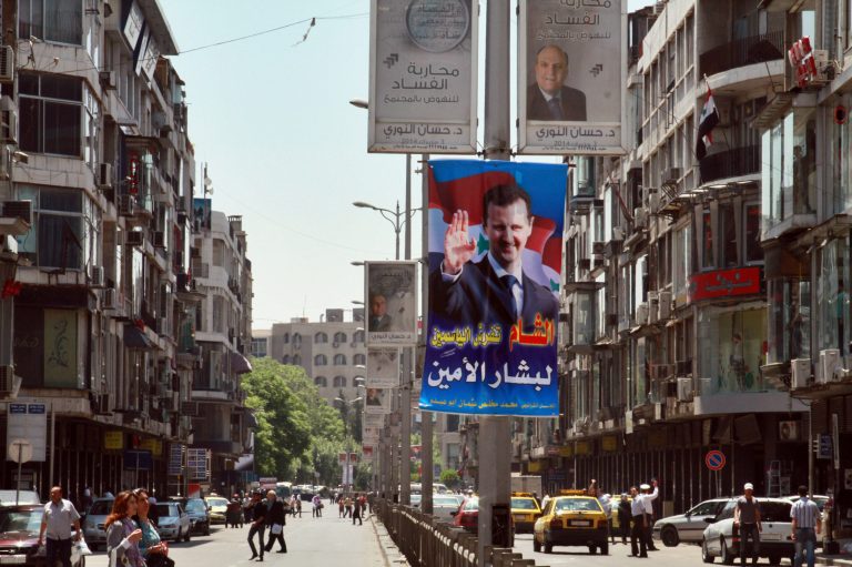Syrians walk on a street decorated with campaign posters of the June 3 presidential election in Damascus, Syria, Monday, May 12, 2014. The Arabic, top center, reads, 
