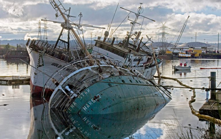 A spill response team wraps a second boom around two old steel ships that sank while moored at Mason Marine Services on the Hylebos Waterway in Tacoma, Wash. (AP/ The News Tribune, Peter Haley)
