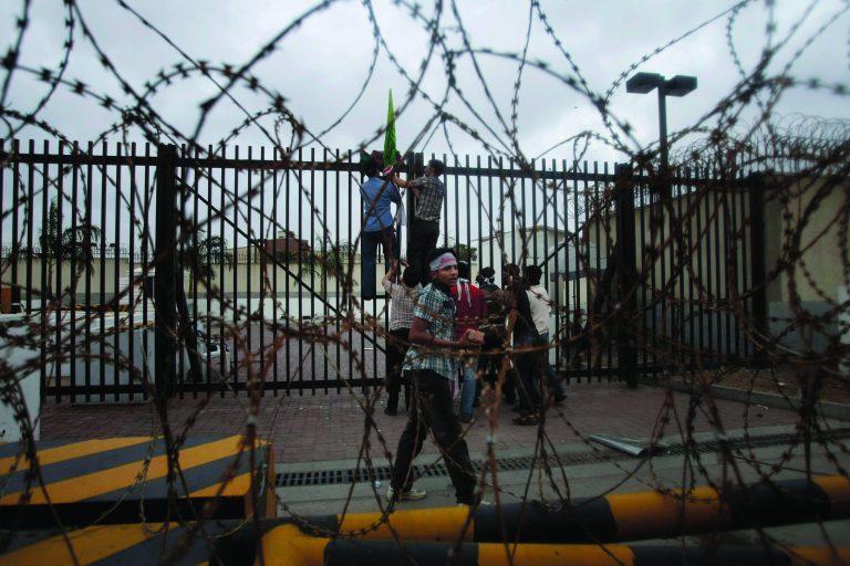 A Pakistani protester holds stone as others hang a flag at the entry of the gate of the U.S. consulate during a demonstration in Karachi, Pakistan, Sunday, Sept. 16, 2012. Hundreds of Pakistanis protesting an anti-Islam video produced in the United States clashed with police Sunday as they tried to march toward the U.S. Consulate in the southern city of Karachi, while thousands of others held peaceful demonstrations in other parts of the country. (AP Photo/Fareed Khan)