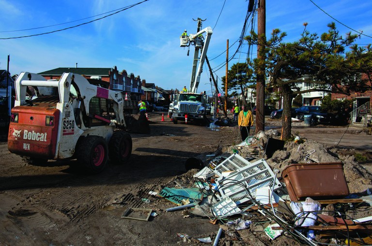 A crew with Salt River Project of Arizona (SRP) works on replacing a pole on a sand and debris-covered street in the Belle Harbor neighborhood of the borough of Queens, New York, Monday, Nov.12, 2012, in the wake of Superstorm Sandy. SRP is one of several out of the region utility companies aiding local utilities. (AP Photo/Craig Ruttle)