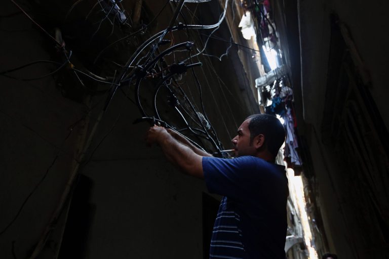 In this May 24, 2014 photo, Abu Wadiyeh, a 34-year-old Palestinian who was born in Syria, fixes power cables at the Palestinian refugee camp of Shatila in Beirut, Lebanon. One look at the jumbled mass of sinewy electricity cables, TV and Internet lines that droop over the damp, narrow alleyways of the Palestinian refugee camp of Shatila, and it's easy to see why. Wadiyeh, chief electrician in Shatila, is responsible for making order out of that chaos to ensure that the camp's more than 20,000 residents can turn on their lights and televisions. (AP Photo/Bilal Hussein)