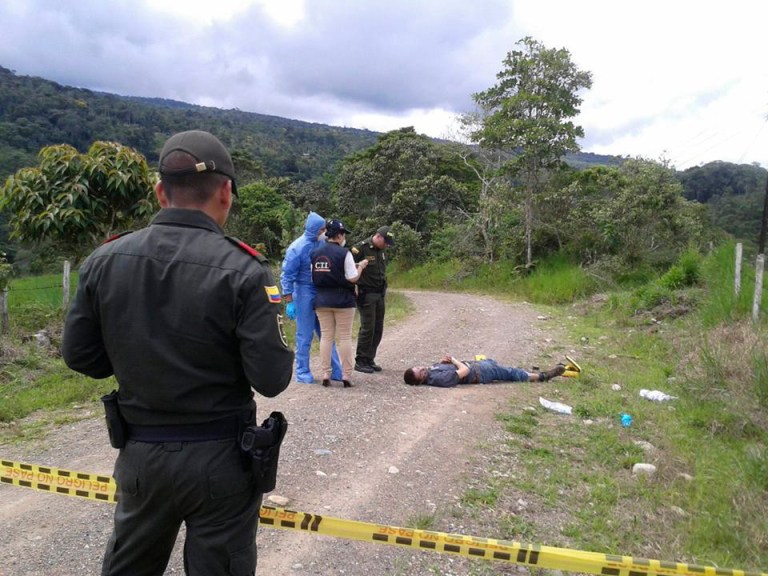 In this photo taken Wednesday, April 23, 2014, police officers and forensics look at the body of British citizen Henry Miller, 19, on a road outside Mocoa, in Colombia's southwestern state of Putumayo. Miller died  after he drank a hallucinogen during a tribal ritual, his body left by the side of the road by two frightened young local men, said Saturday local police commander Ricardo Suarez. (AP Photo/Jose Horacio Villarreal)