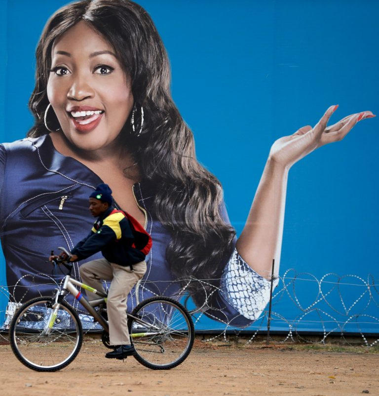 A man cycles past a billboard featuring Sophie Ndaba, an actor who played the Queen Moroka character in 