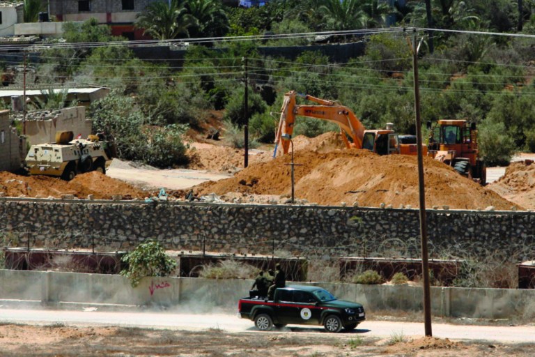In this Wednesday, Aug. 22, 2012 photo, Palestinian Hamas border guards patrol the Egyptian Gaza border while an Egyptian bulldozer works on the demolition of a smuggling tunnel, as seen from Rafah, southern Gaza Strip. Hamas had hoped the Islamists who took charge in Egypt this summer -- fellow members of the region's Muslim Brotherhood -- would swiftly turn the shared border crossing into a free-flowing trade route, ending Gaza's five-year isolation from the world and making the tunnels obsolete. (AP Photo/Eyad Baba)