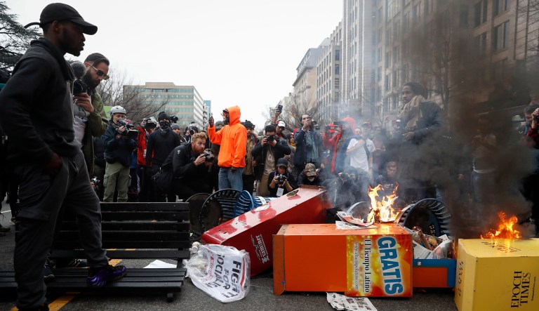 A Washington resident, left, guards a pile of burning newspaper machines to prevent protestors from feeding the flames while demanding peace in the streets during a demonstration after the inauguration of President Trump, Friday, Jan. 20, 2017, in Washington. (AP Photo/John Minchillo)