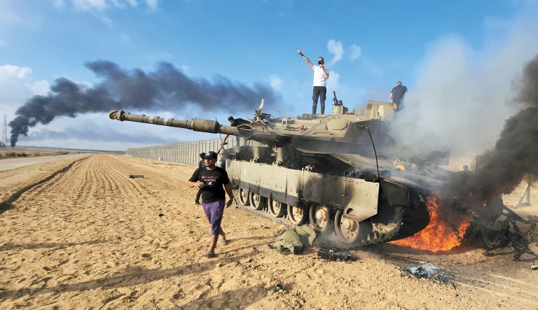 Palestinians celebrate by a destroyed Israeli tank at the Gaza Strip fence east of Khan Younis on Oct. 7.Â 