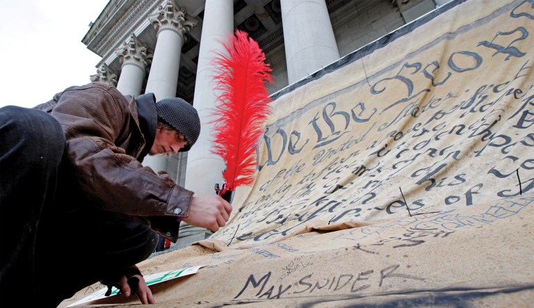 A protester against budget cuts signs his name to a giant copy of the U.S. Constitution in Olympia, Washington on Nov. 28, 2011.