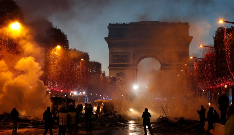 Plumes of smoke are seen near the Arc de Triomphe on the Champs-Elysees avenue decorated with the Christmas lightings during a protest against tax Saturday, Nov. 24, 2018 in Paris. French police fired tear gas and water cannons to disperse violent demonstrators in Paris, as thousands gathered in the capital and beyond and staged road blockades to vent anger against rising fuel taxes.
