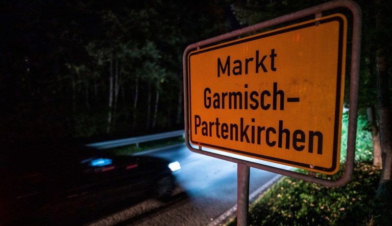 FILE-In this Sept. 13, 2020 taken photo a car drives past the place name sign in Garmisch-Partenkirchen, Germany. Officials in southern Germany are considering imposing hefty fines against a 26-year-old American woman linked to a cluster of coronavirus cases in the Alpine resort town of Garmisch-Partenkirchen, including at a hotel that caters to U.S. military personnel.