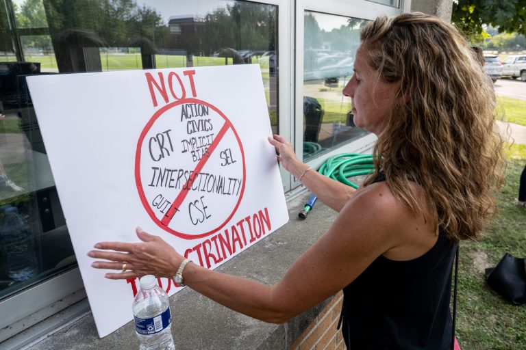 A demonstrator props up a sign during a protest against critical race theory before a school board meeting.