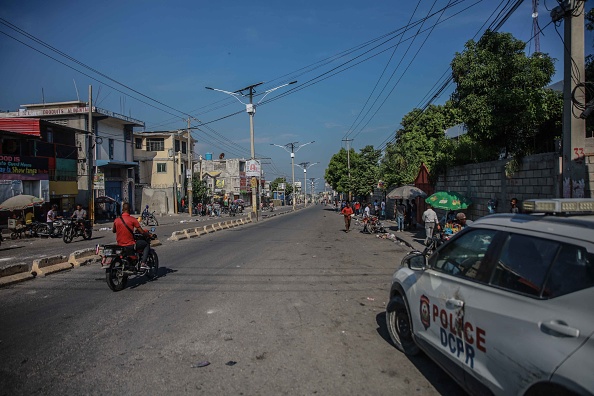 People ride a motorcycle past a police car in Port-au-Prince on October 18, 2021. - The kidnapping of 17 adults and children by one of Haiti's brazen criminal gangs underlined the country's troubles following the assassination of president Jovenel Mose in July.