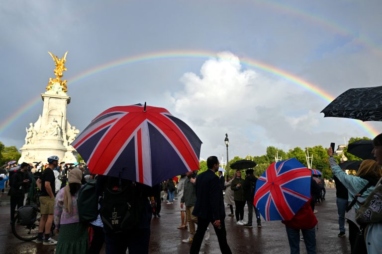 A man looks on as a rainbow is seen outside of Buckingham Palace.