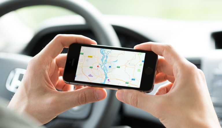 Man in the car planning a route using a Google Maps application on Apple iPhone 5S. Google Maps is a most popular web mapping service for mobile provided by Google inc.
