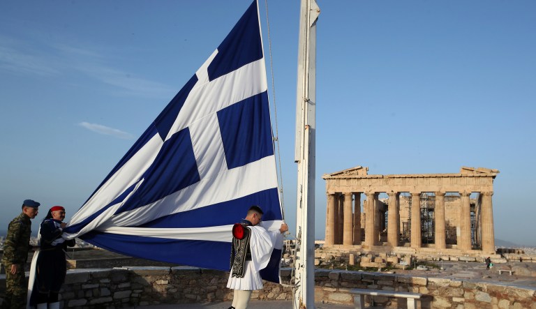 In this Sunday, April 1, 2018, photo members of the Presidential Guard raising the Greek flag in front of the Parthenon temple atop of Acropolis Hill in Athens. Created 150 years ago as a fighting force that distinguished itself in a series of wars, the unit is now purely ceremonial in function, codifying in its dress and routine a popular conception of Greekness that evolved since the modern Greek state was formed nearly two centuries ago.