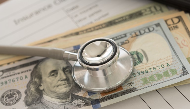 Health insurance claim concept. Stethoscope on dollar banknote with calculator, health insurance claim form on desk.