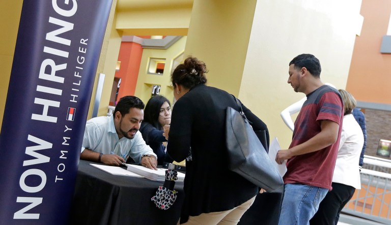 In this Tuesday, Oct. 3, 2017, file photo, job seekers stand at a booth at a job fair at the Dolphin Mall in Sweetwater, Fla.