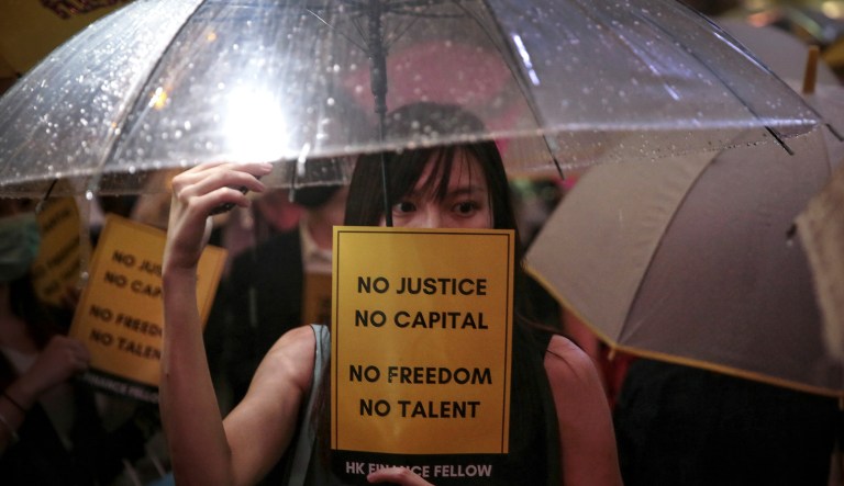 A woman holds an umbrella and a placard as people gather at Chater Garden to give support to the recent protests against the extradition bill, at the financial district in Hong Kong, Thursday, Aug, 1, 2019.