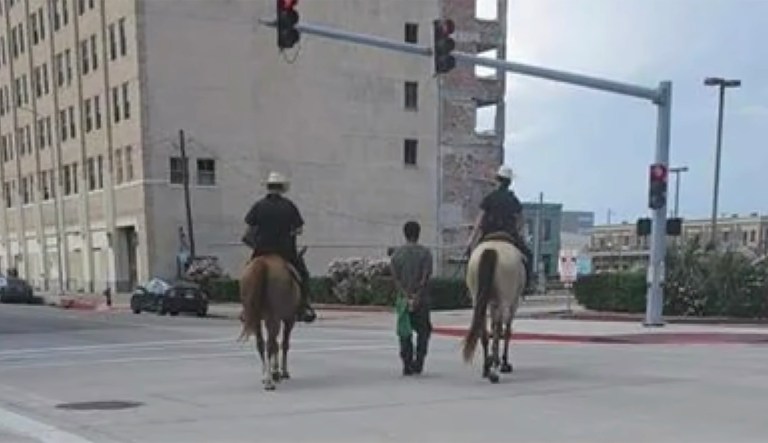 Mounted police lead suspect through street by rope.