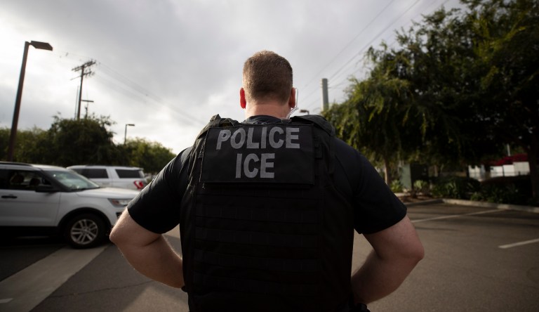 In this July 8, 2019, photo, a U.S. Immigration and Customs Enforcement (ICE) officer looks on during an operation in Escondido, Calif. The carefully orchestrated arrest last week in this San Diego suburb illustrates how President Donald Trump's pledge to start deporting millions of people in the country illegally is virtually impossible with ICE's budget and its method of picking people up.