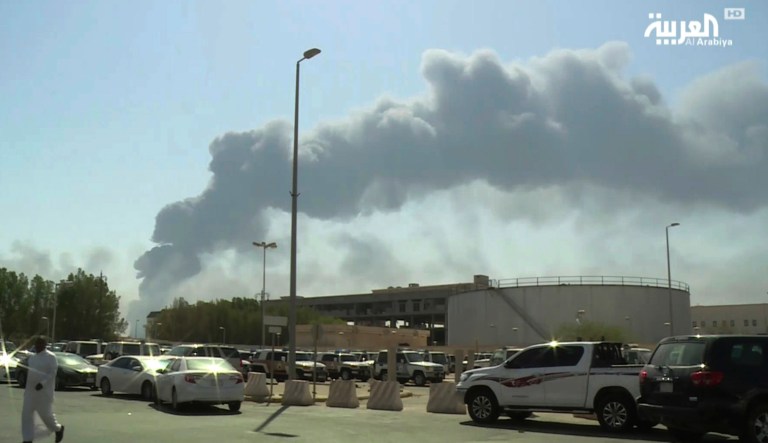 In this Saturday, Sept. 14, 2019 file photo made from a video broadcast on the Saudi-owned Al-Arabiya satellite news channel, a man walks through a parking lot as the smoke from a fire at the Abqaiq oil processing facility can be seen behind him in Buqyaq, Saudi Arabia.