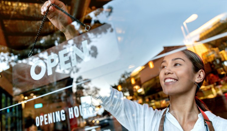 A woman rotates a sign to say that a store is open.