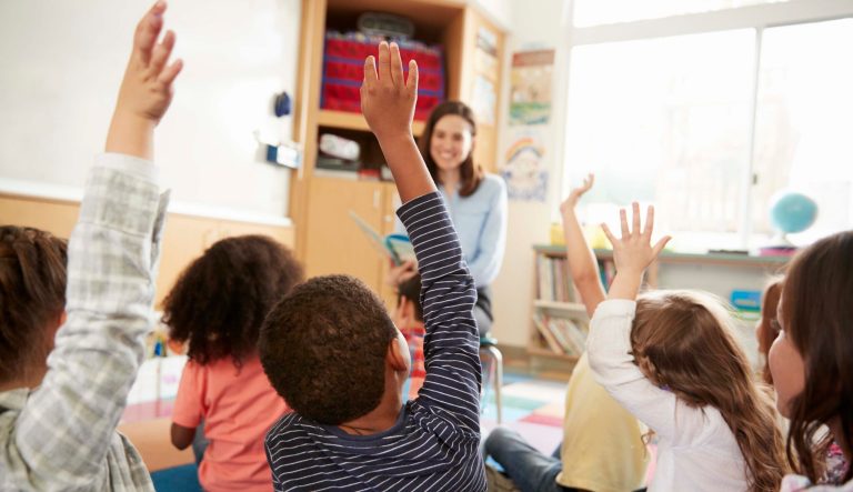 Elementary school kids raising their hands to their teacher.
